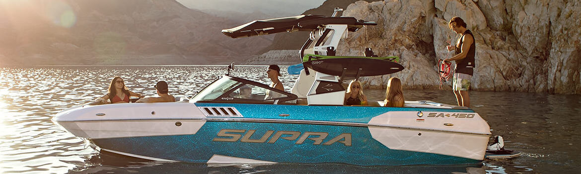 A group of people hanging out on a Supra SA boat on the water near a cliff